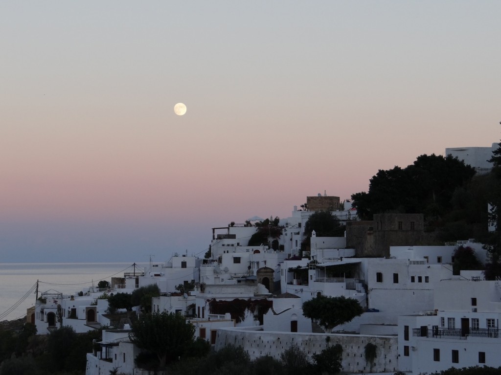 Lindos during sunset. The picture has all of the typical island characteristics: A city full of white houses on a cliff side overlooking the water. 